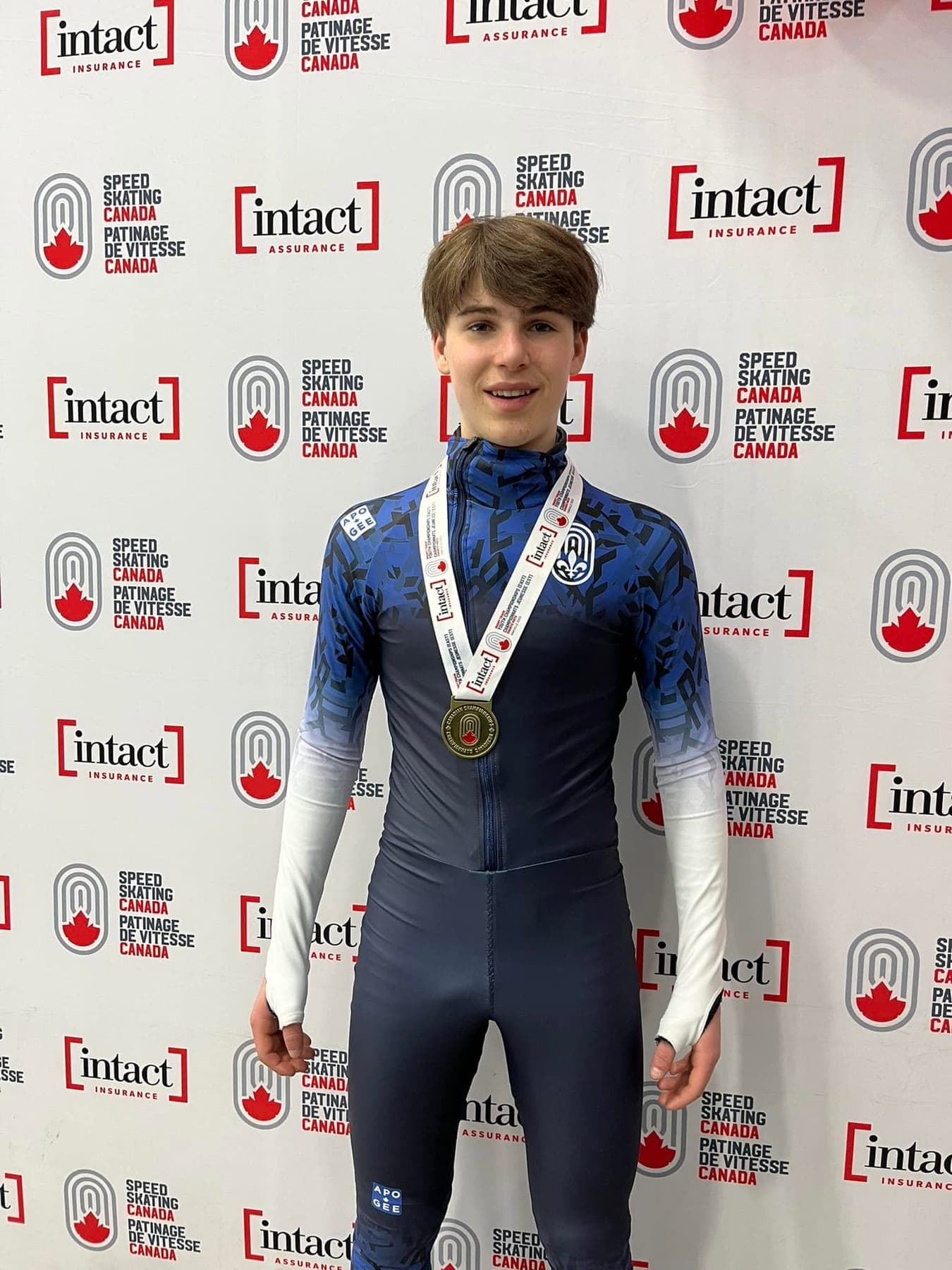 Zac avec sa médaille devant l'affiche de Patinage de vitesse Canada